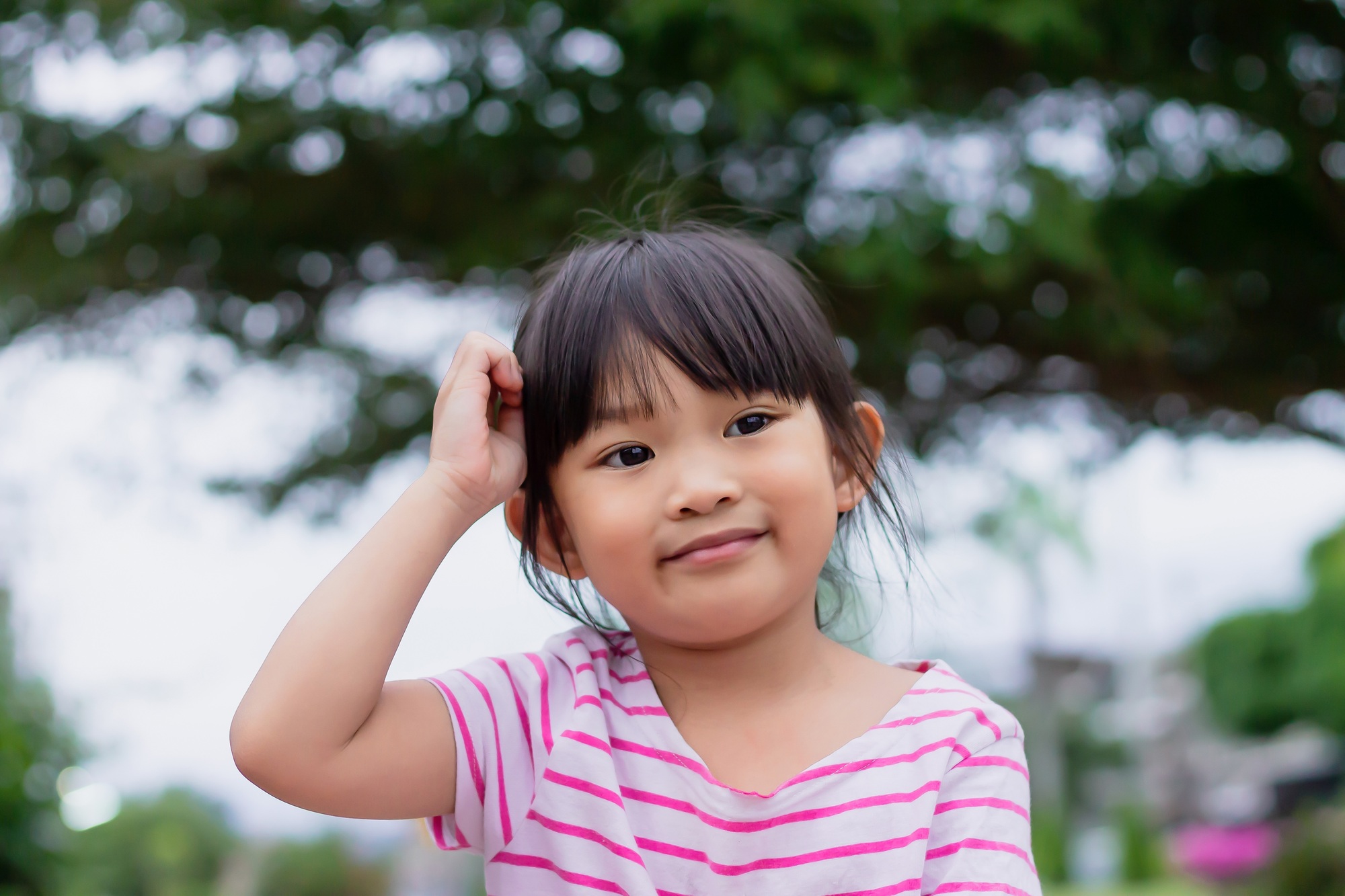 Face of smile and laugh Asian​ girl in head shot. Happy​ kid playing​ at the park playground.