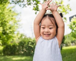 cheerful asian kid standing with raised hands outside
